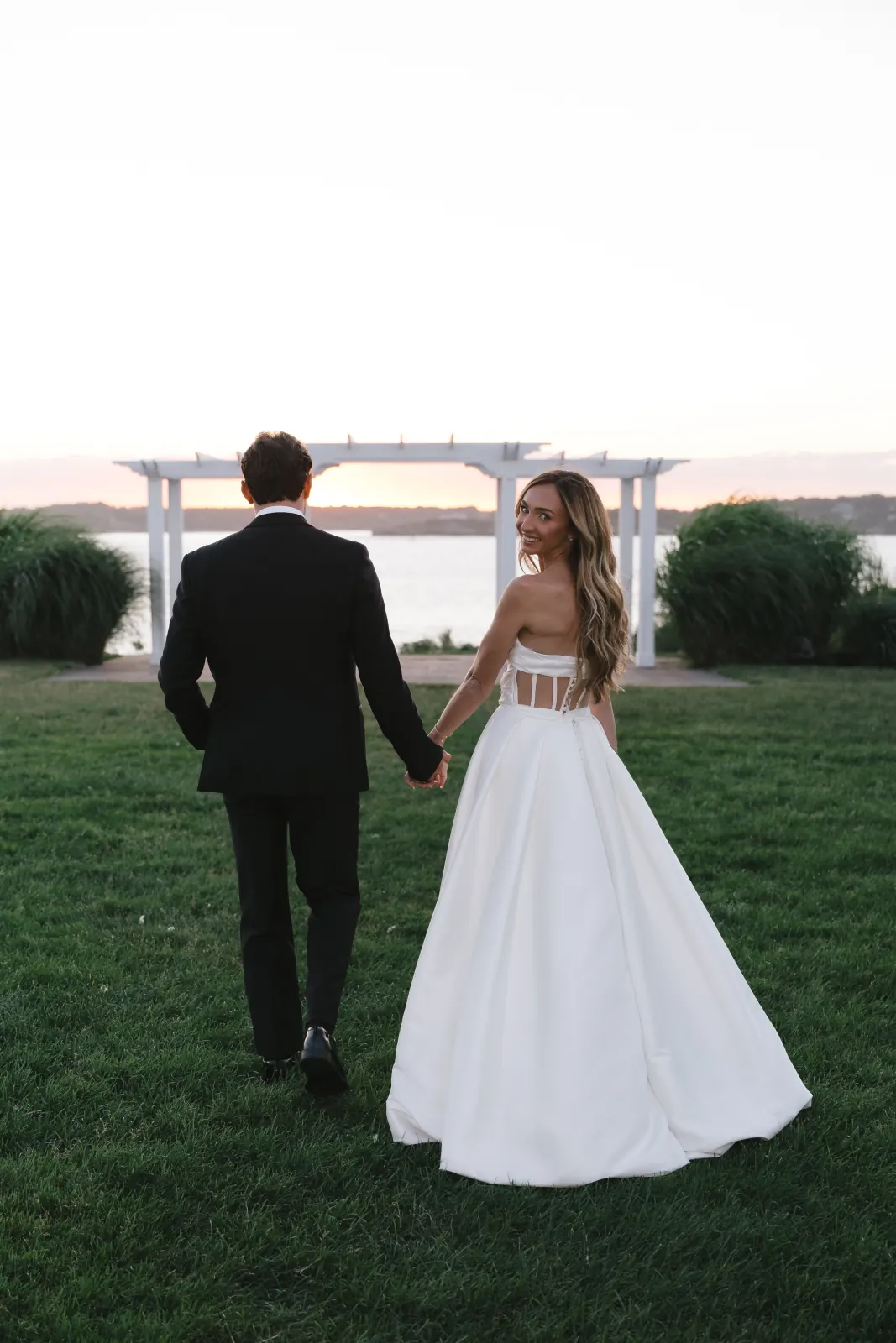 The couple walk toward the bayfront pergola at golden hour, OceanCliff Newport