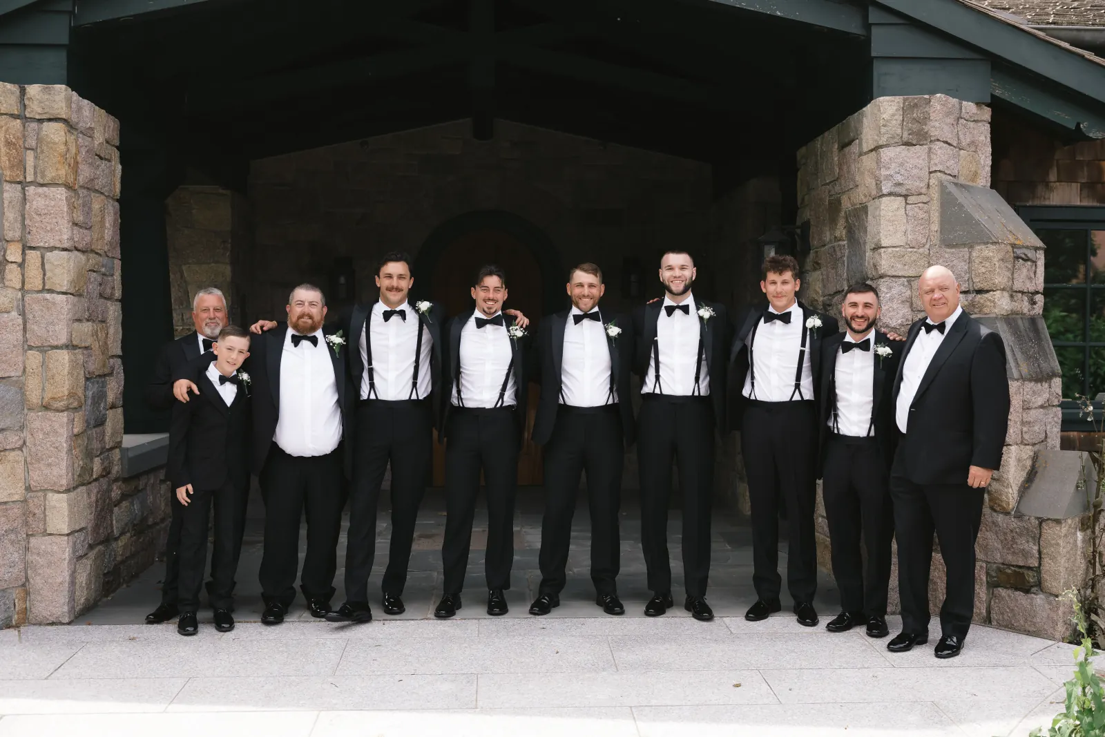 Groom and groomsmen in black tuxedos under the chapel's stone archway