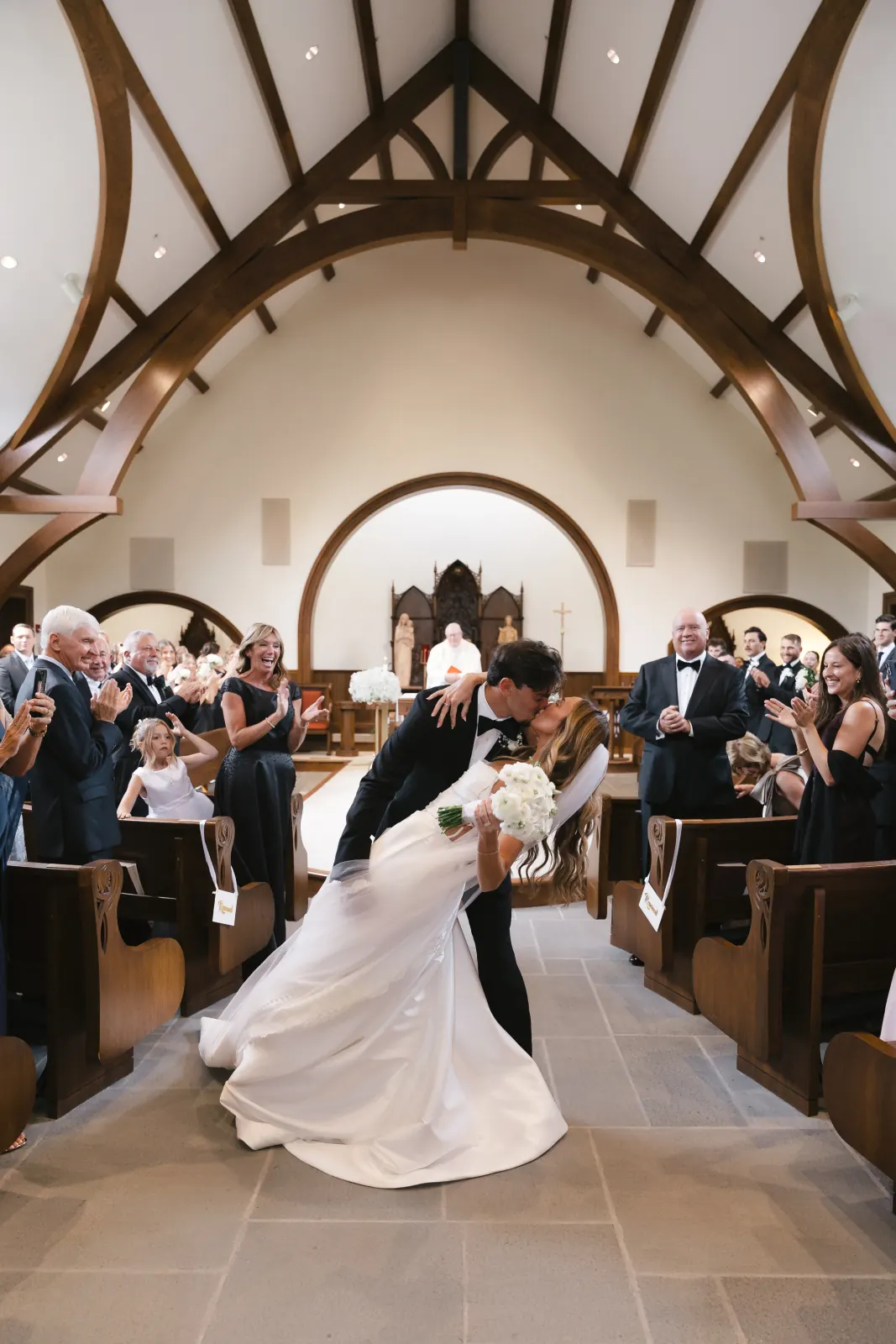 Bride and groom's first kiss and dip in the aisle as the bridal party cheers