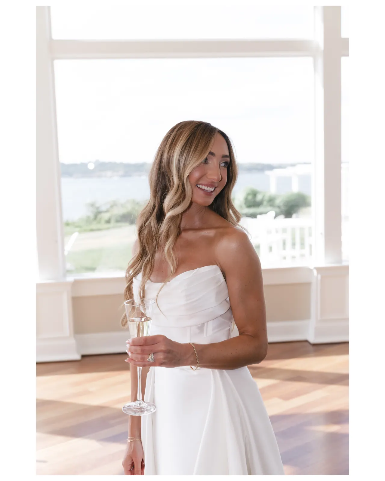Bride with a glass of champagne by the floor-to-ceiling bay windows at OceanCliff