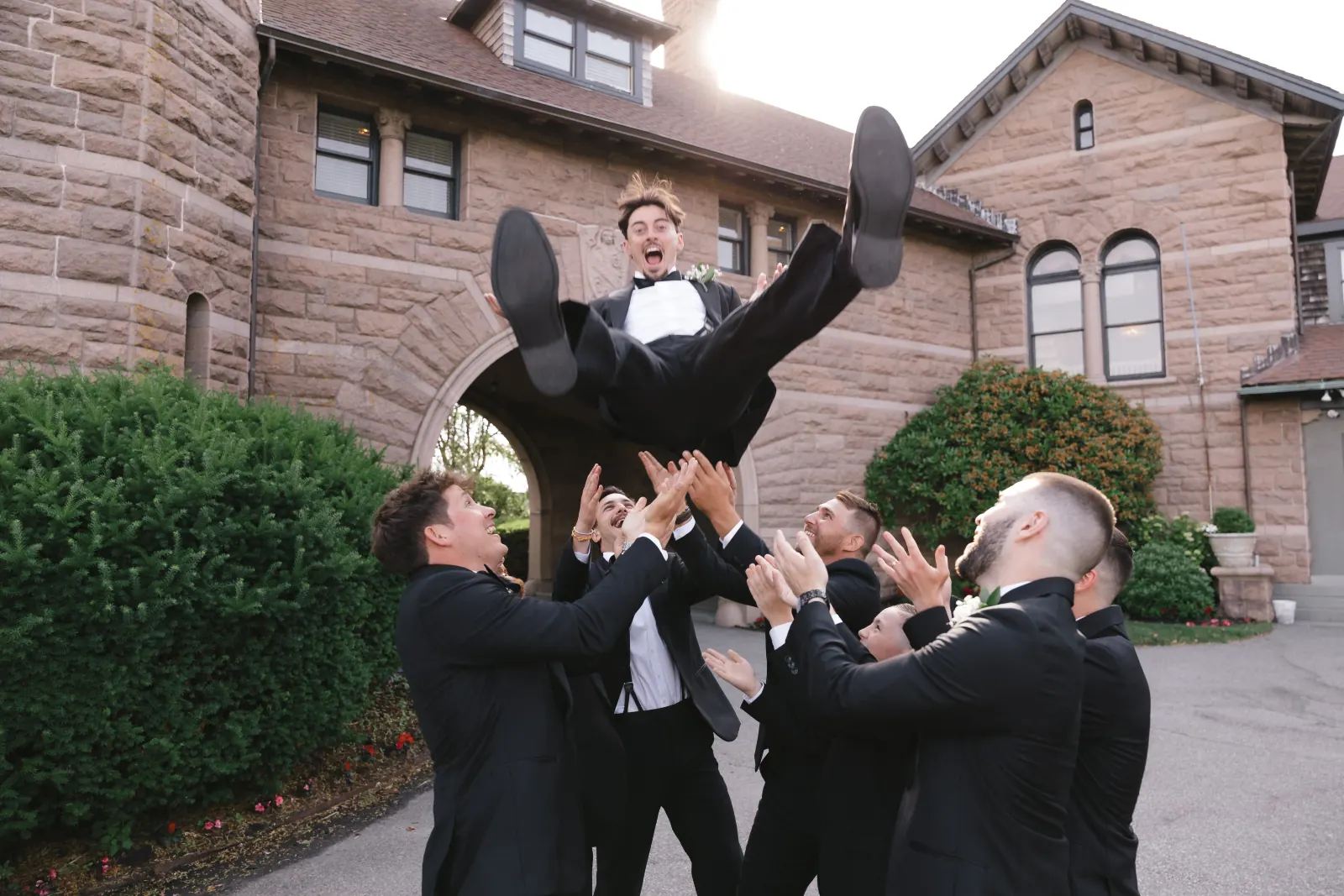 Groomsmen toss the groom in the air outside OceanCliff in Newport