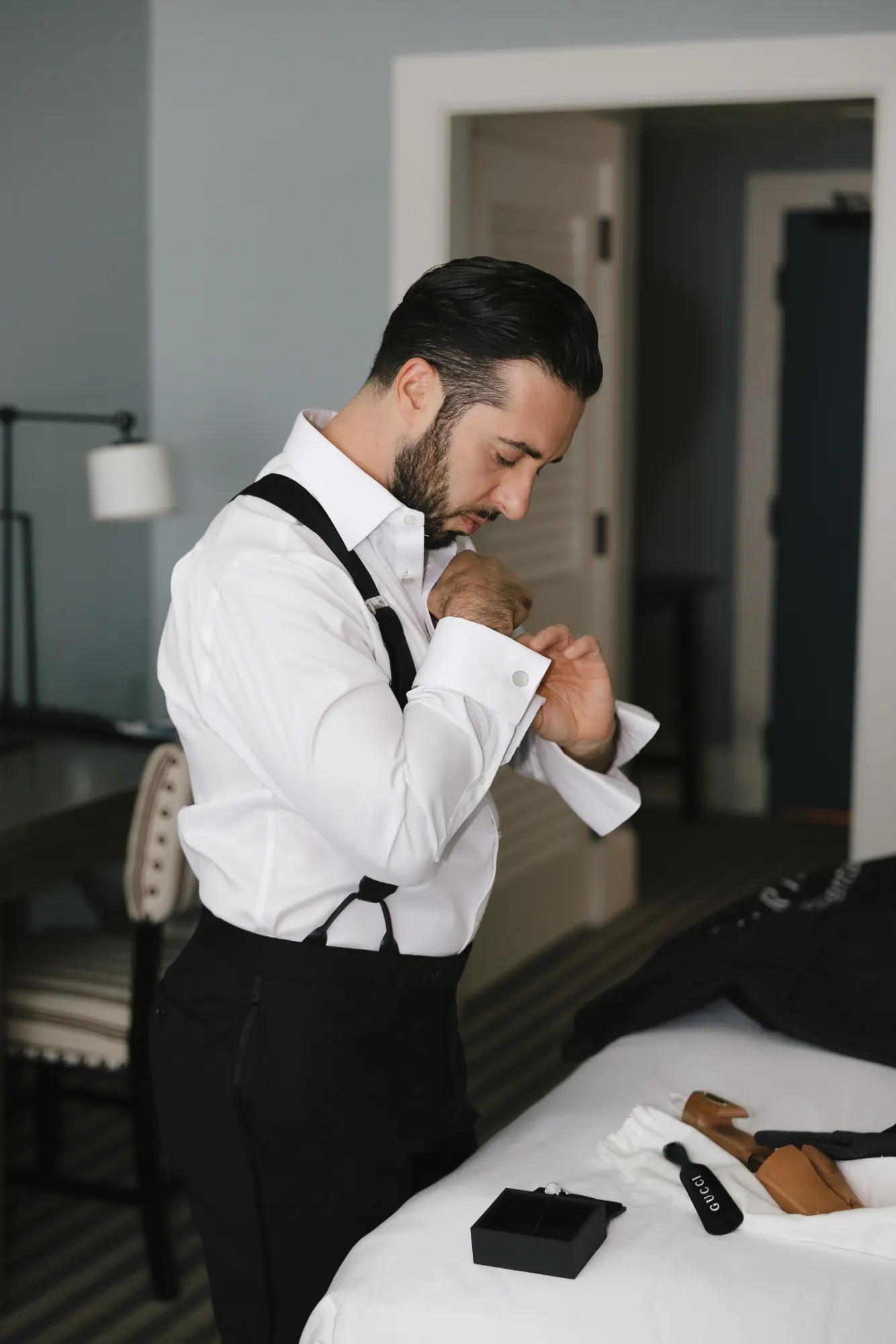 Groom in suspenders fastens his cuff while getting ready at the Beauport Hotel in Gloucester