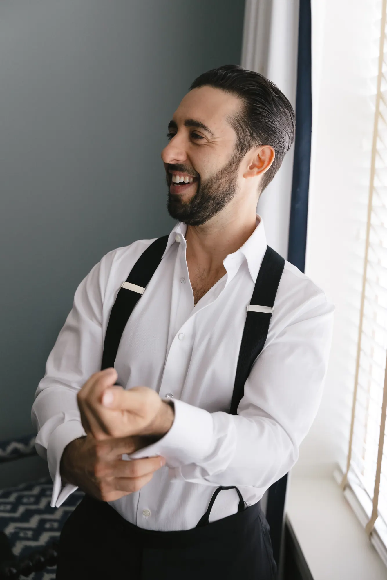 Groom laughs while buttoning his shirt sleeve at the Beauport Hotel