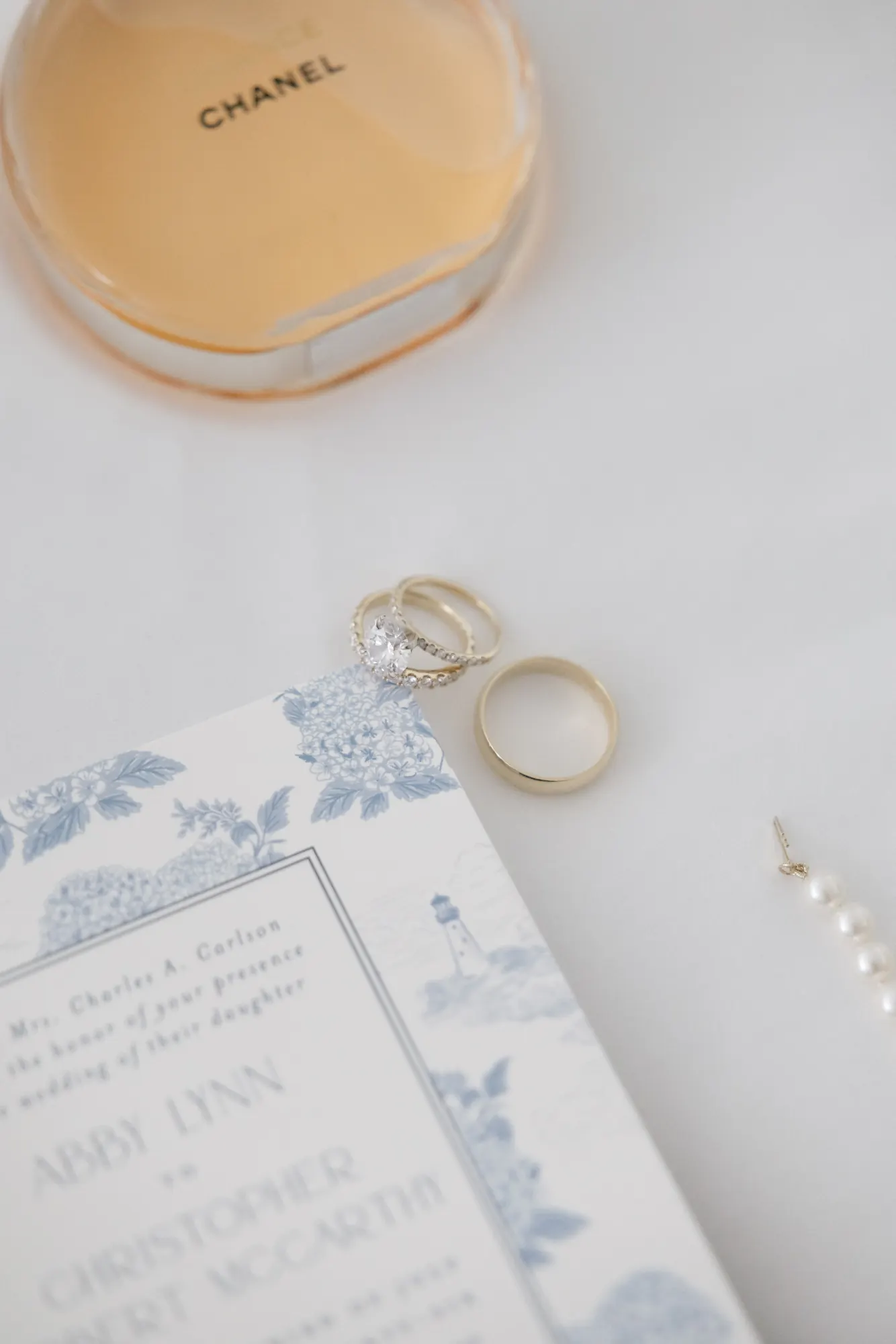 Flat lay of the bride's perfume, rings, pearls, and blue-and-white invitation suite
