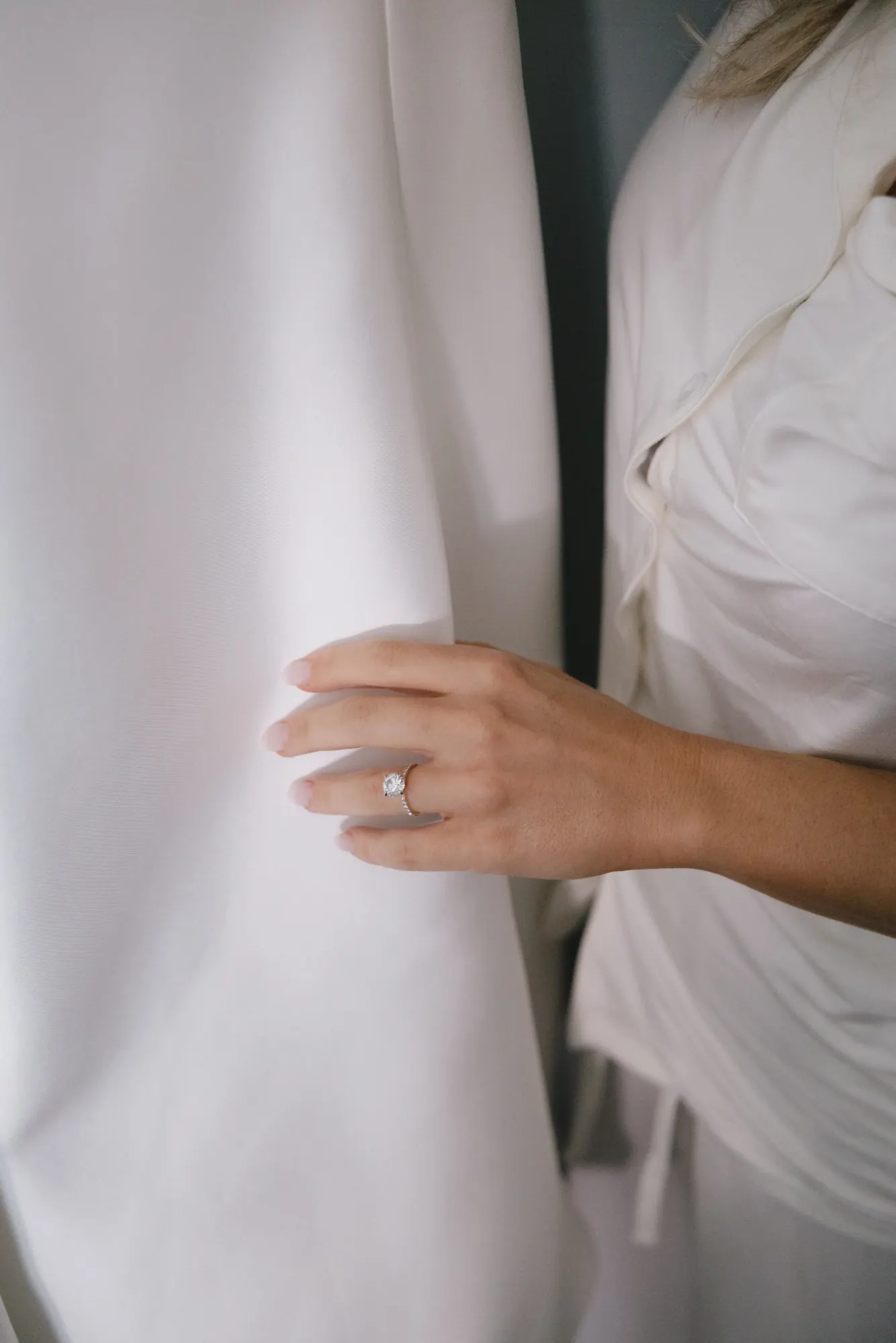 Detail of the bride's hand and engagement ring against her wedding gown
