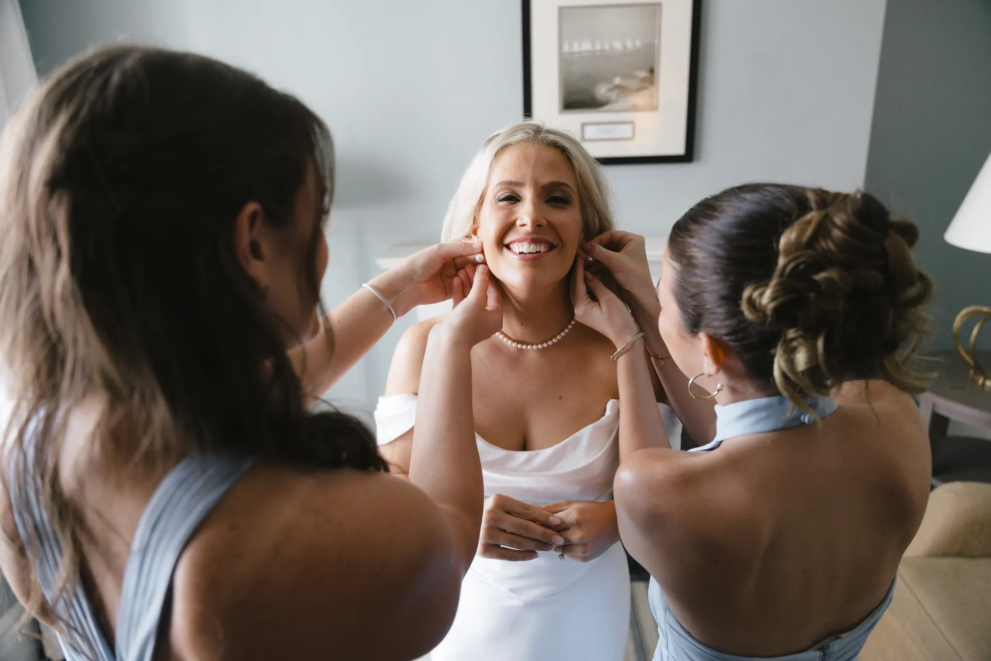 Bridesmaids help the bride with her earrings and pearls