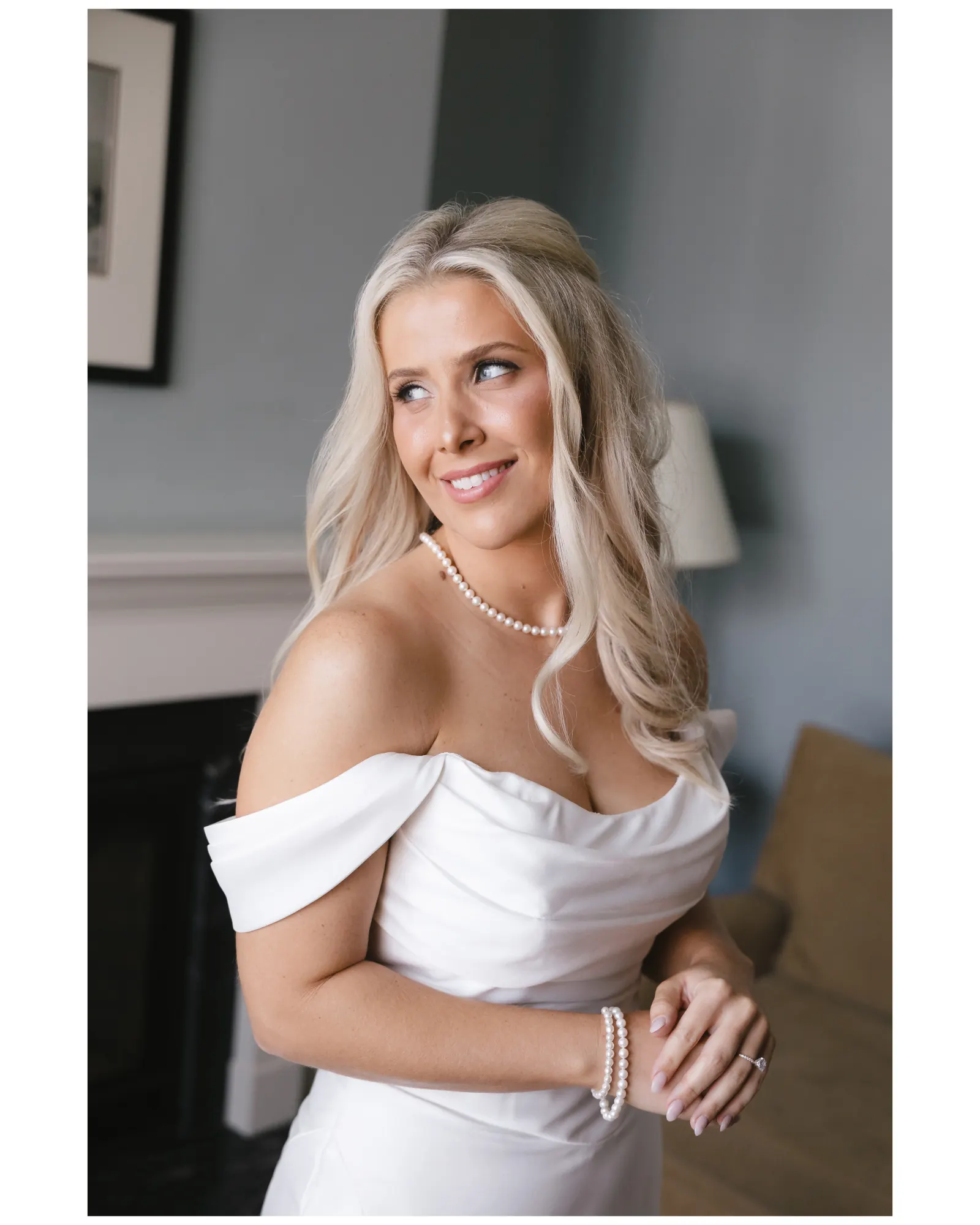 Bride in her off-the-shoulder gown and pearls smiles over her shoulder