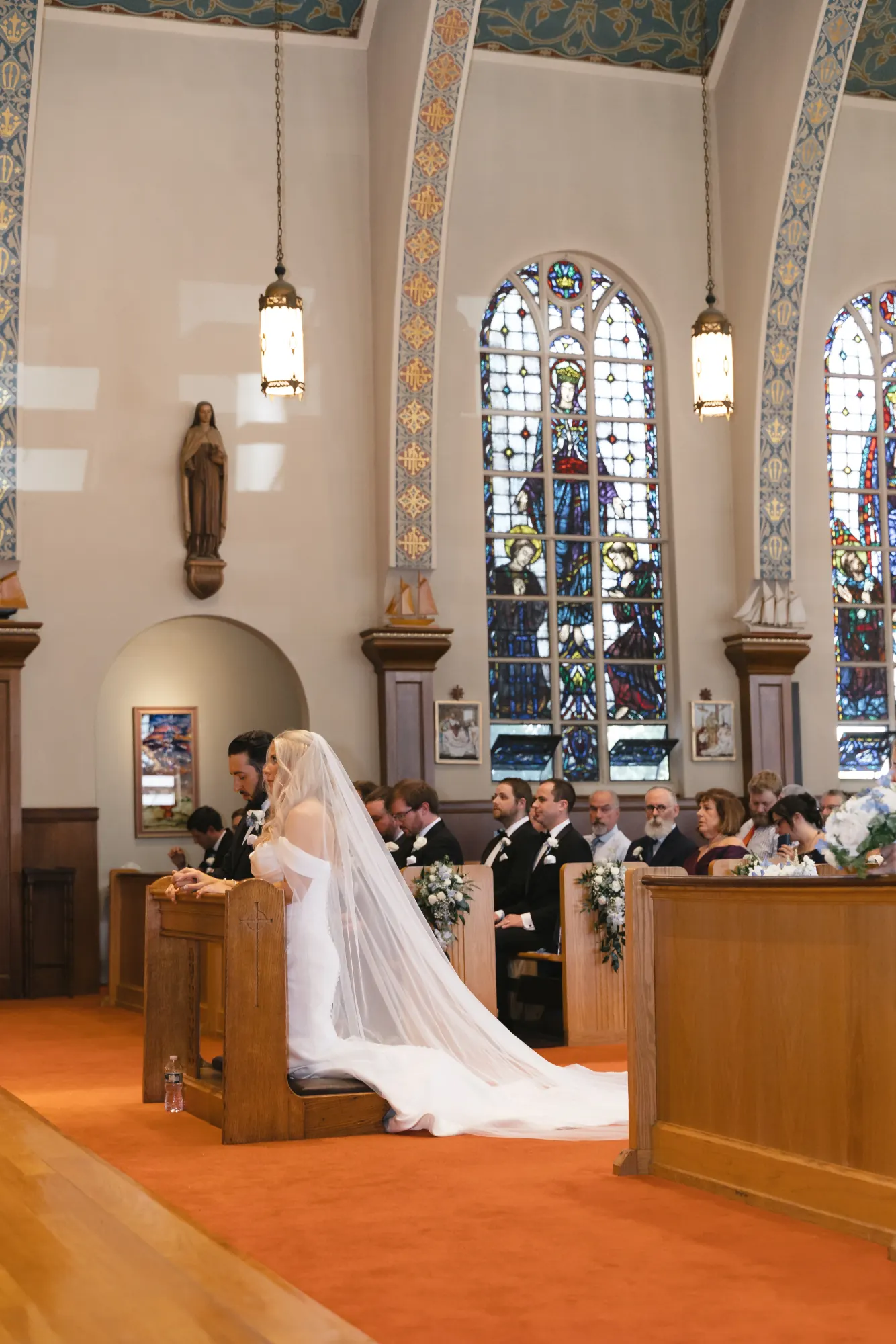 Bride in profile beneath the stained glass windows of Our Lady of Good Voyage