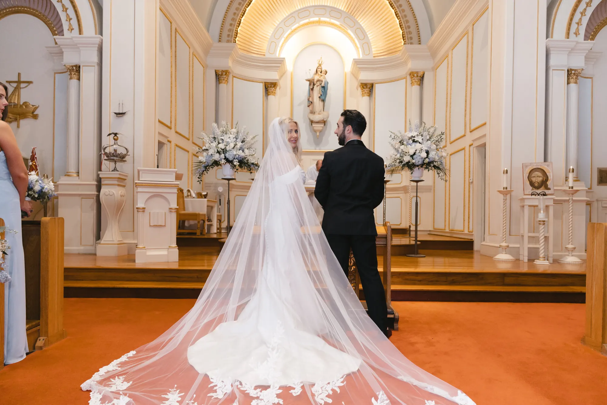 Couple at the altar beneath the gold arch, cathedral veil trailing behind