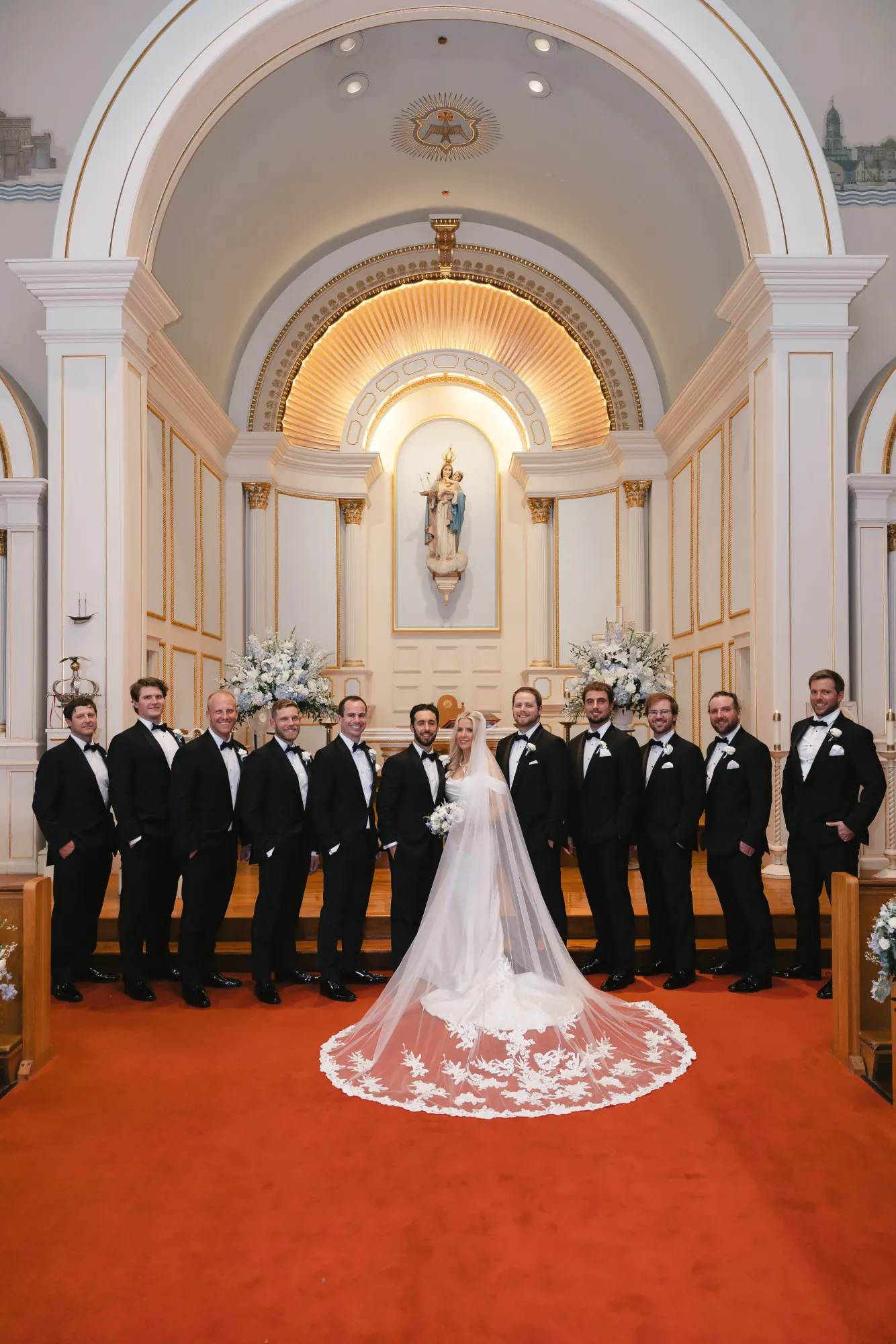 Groom with his groomsmen at the altar, the bride's veil sweeping the red carpet