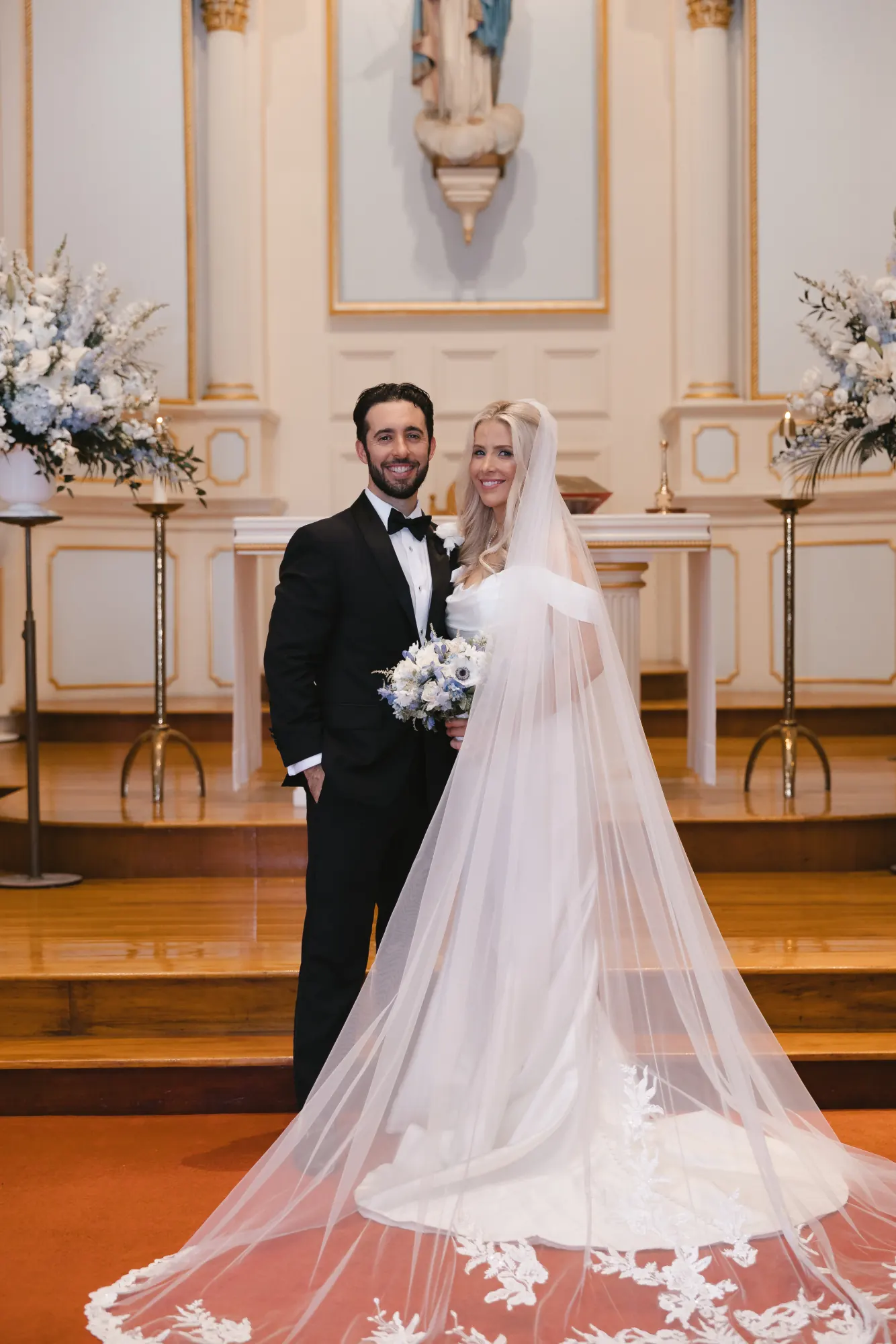 Bride and groom portrait at the altar, her lace cathedral veil spread before them