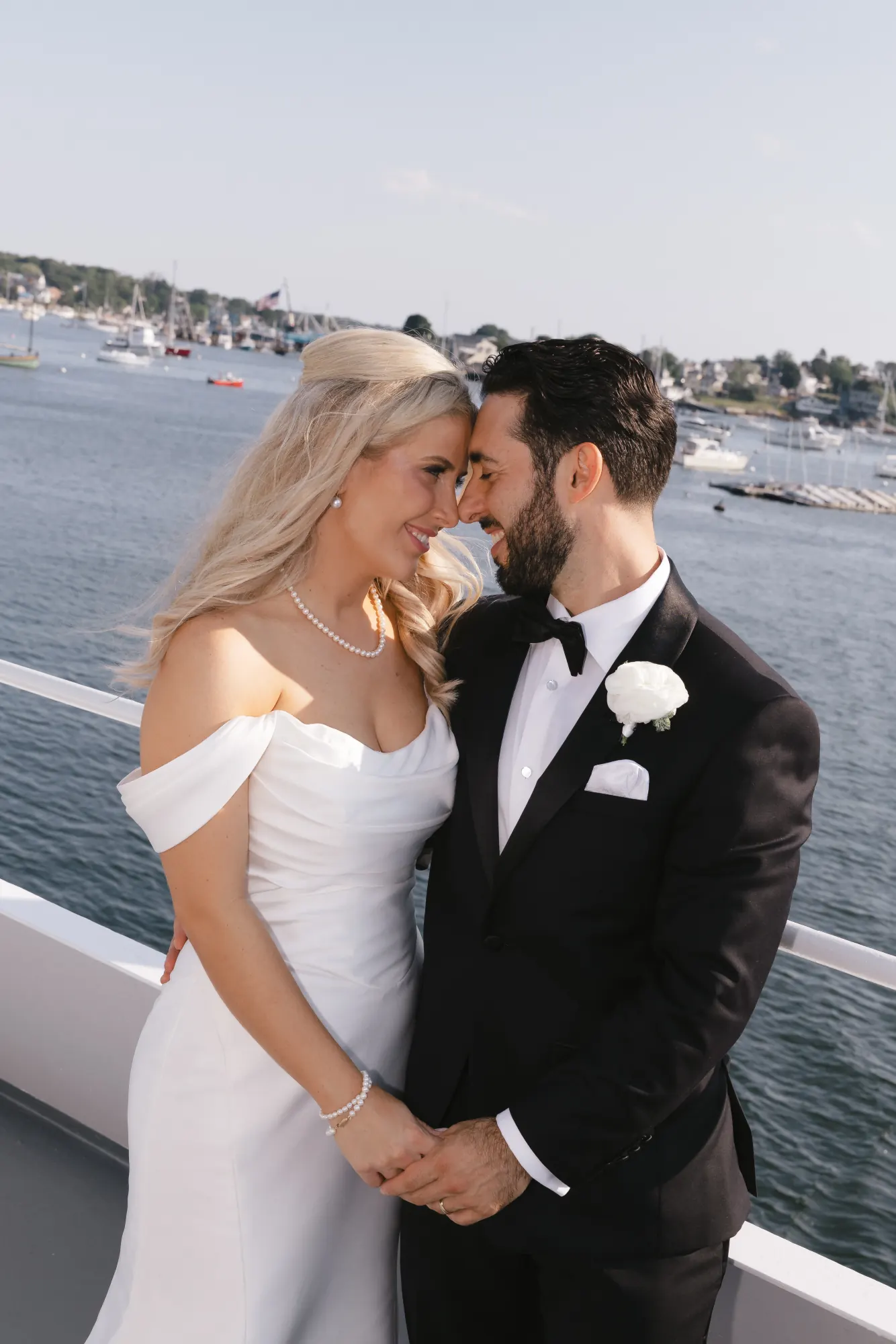 Bride and groom nose to nose at the rail with Gloucester Harbor behind them