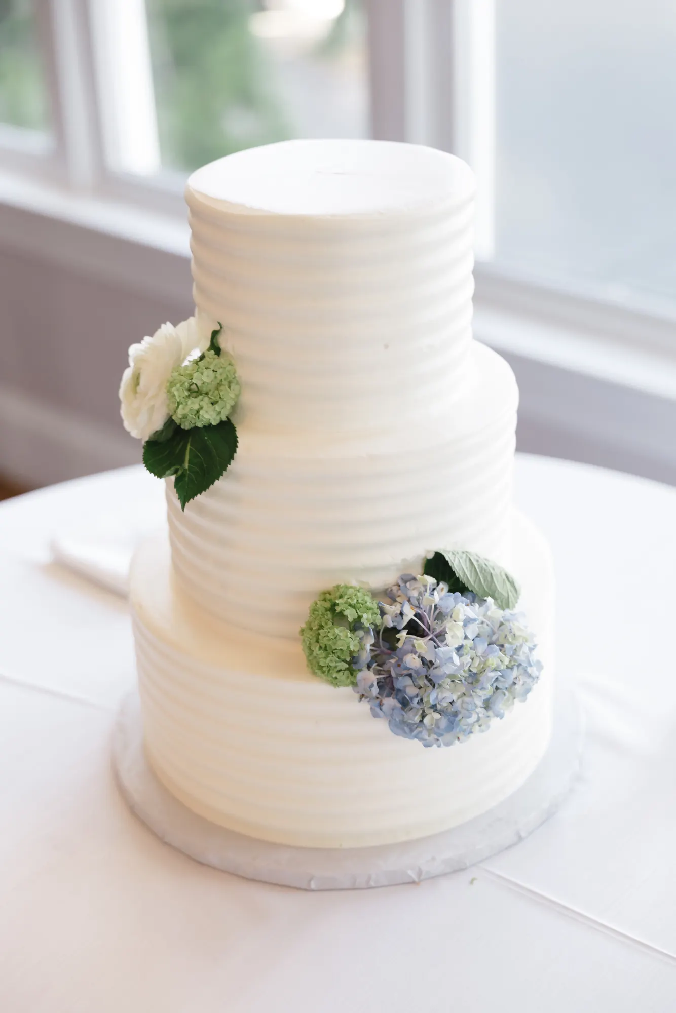 Three-tier white wedding cake with blue hydrangea at Cruiseport Gloucester
