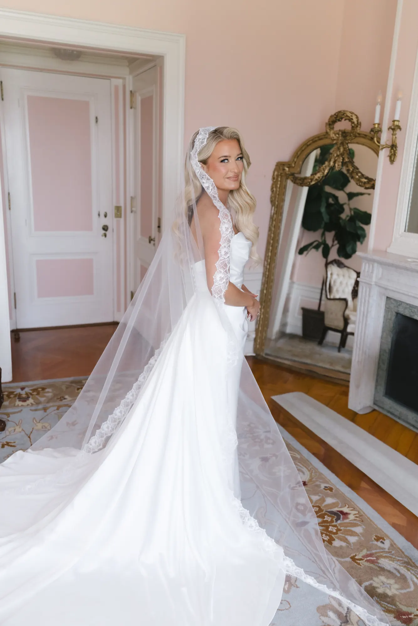 The lace-edged cathedral veil from behind by the bridal suite mirror