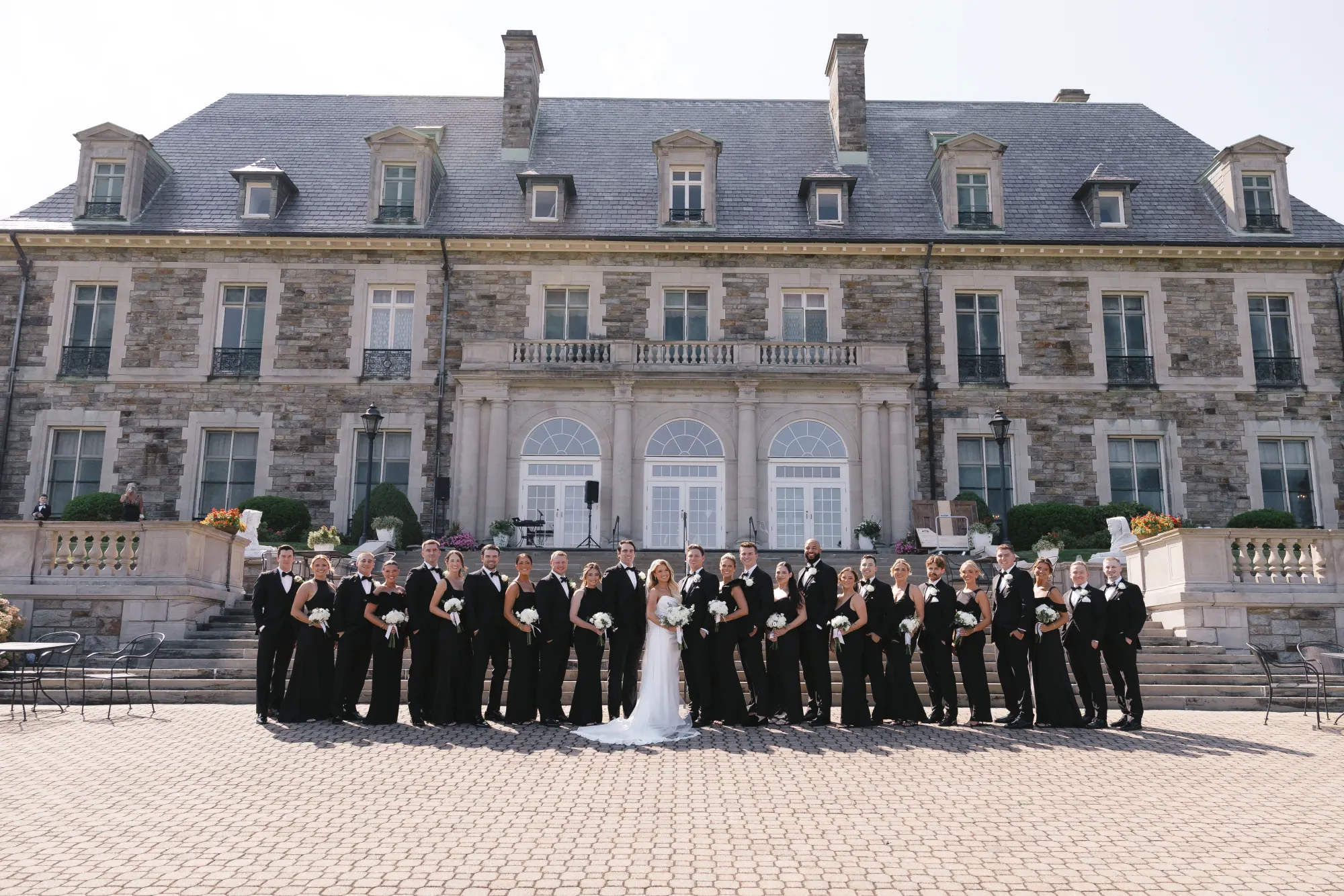 The full wedding party in black in front of the mansion