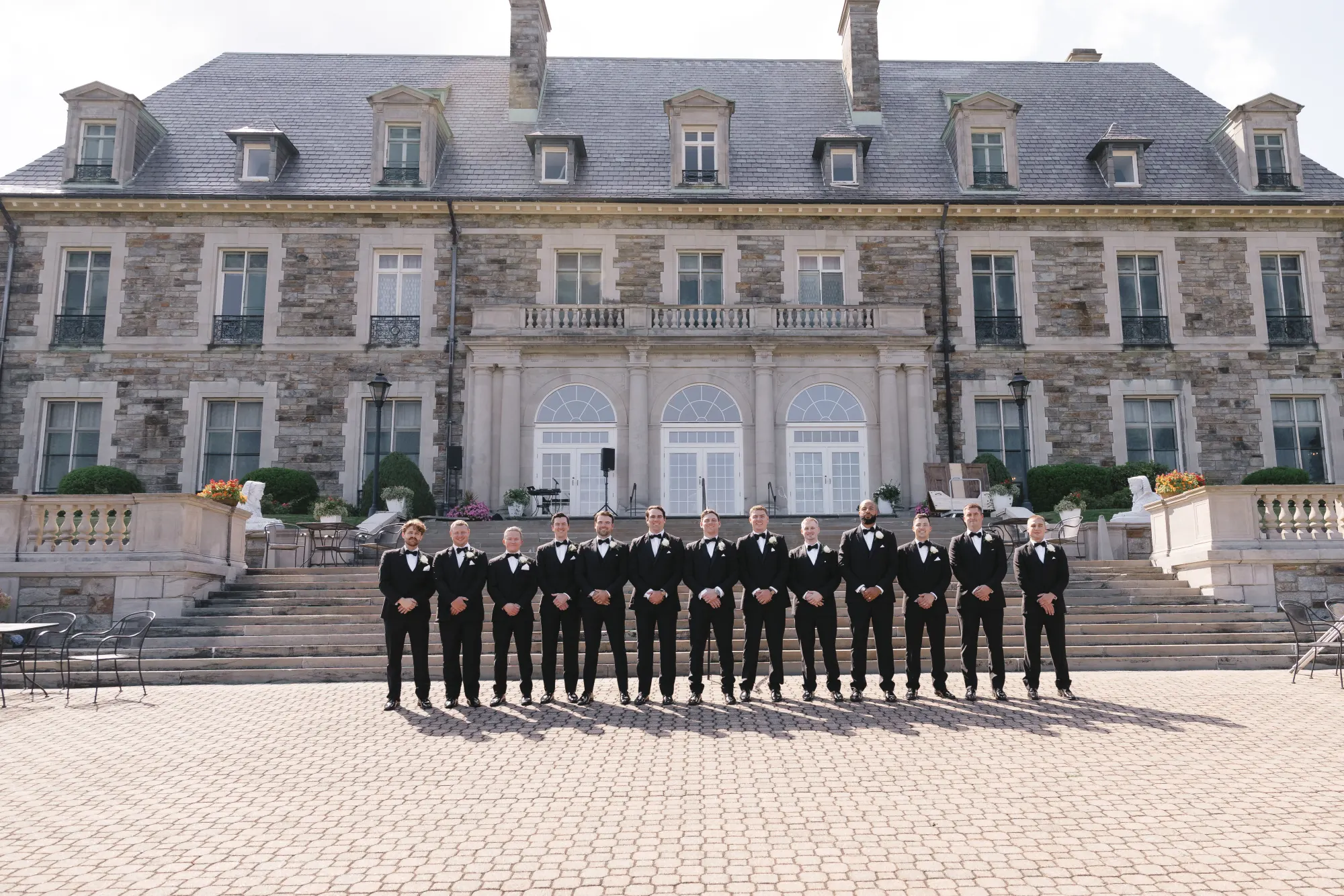 Max and his groomsmen in black tuxedos in front of the mansion