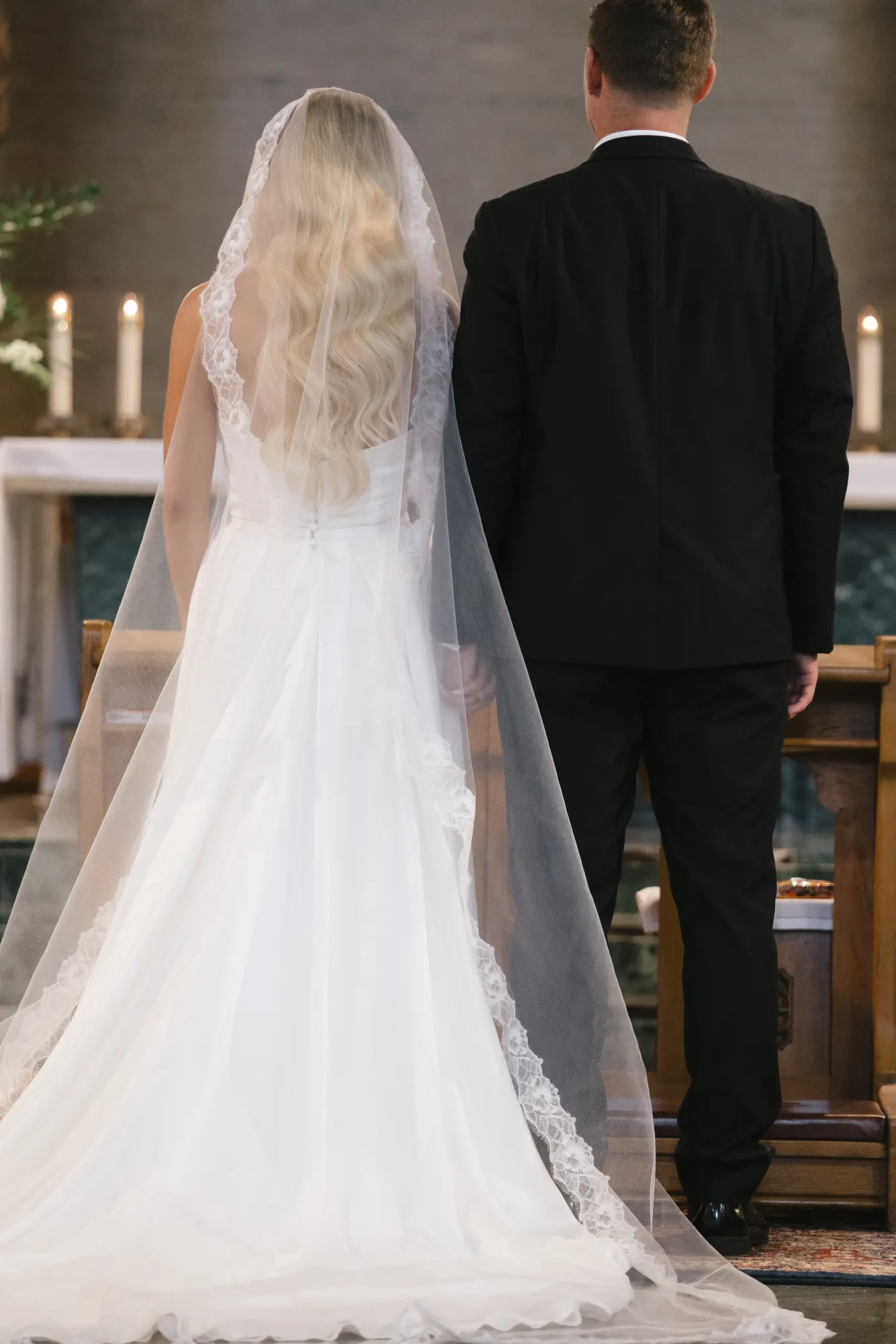 The couple from behind at the altar, veil cascading to the floor