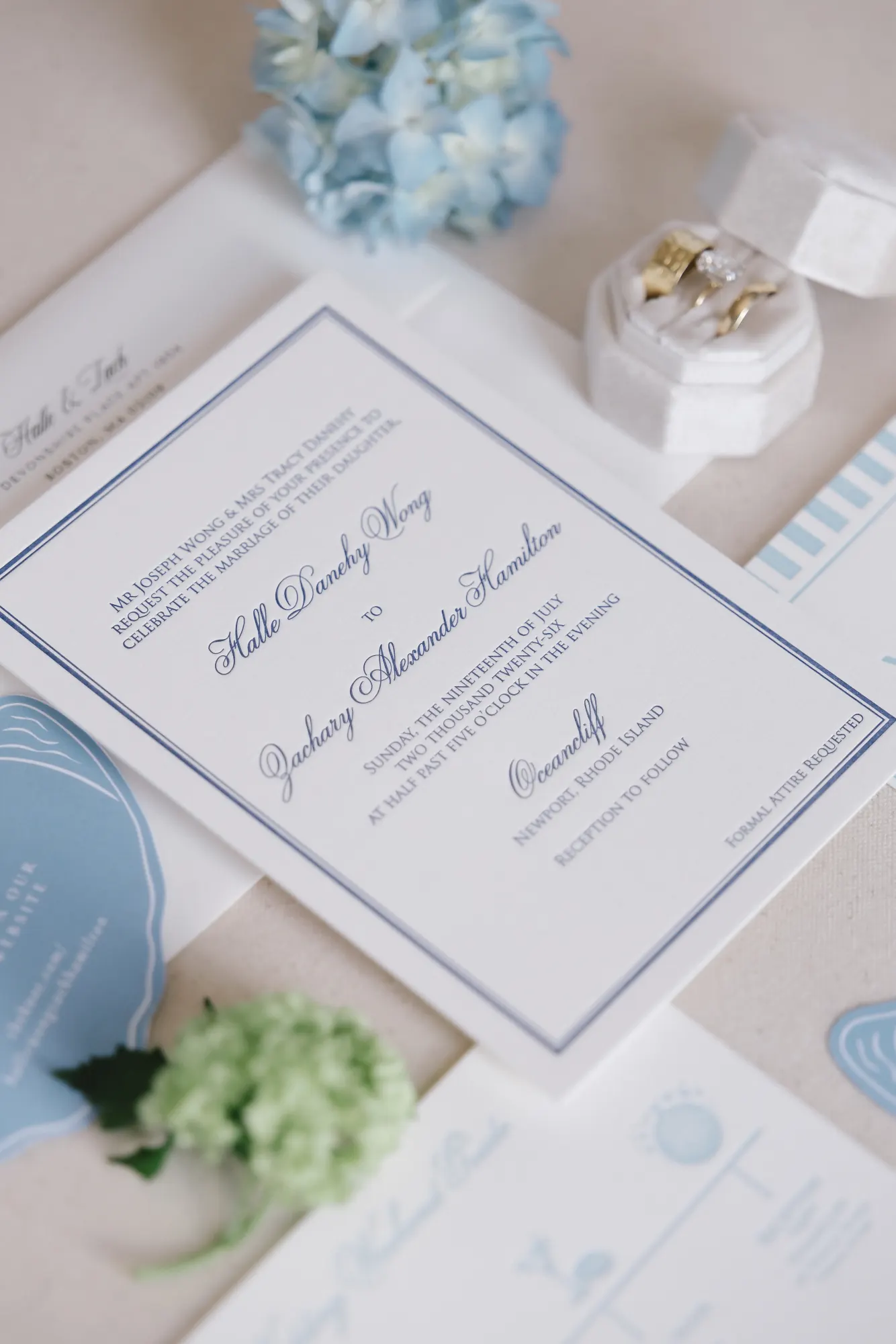 Invitation flat lay with blue hydrangea and the couple's rings in a white box