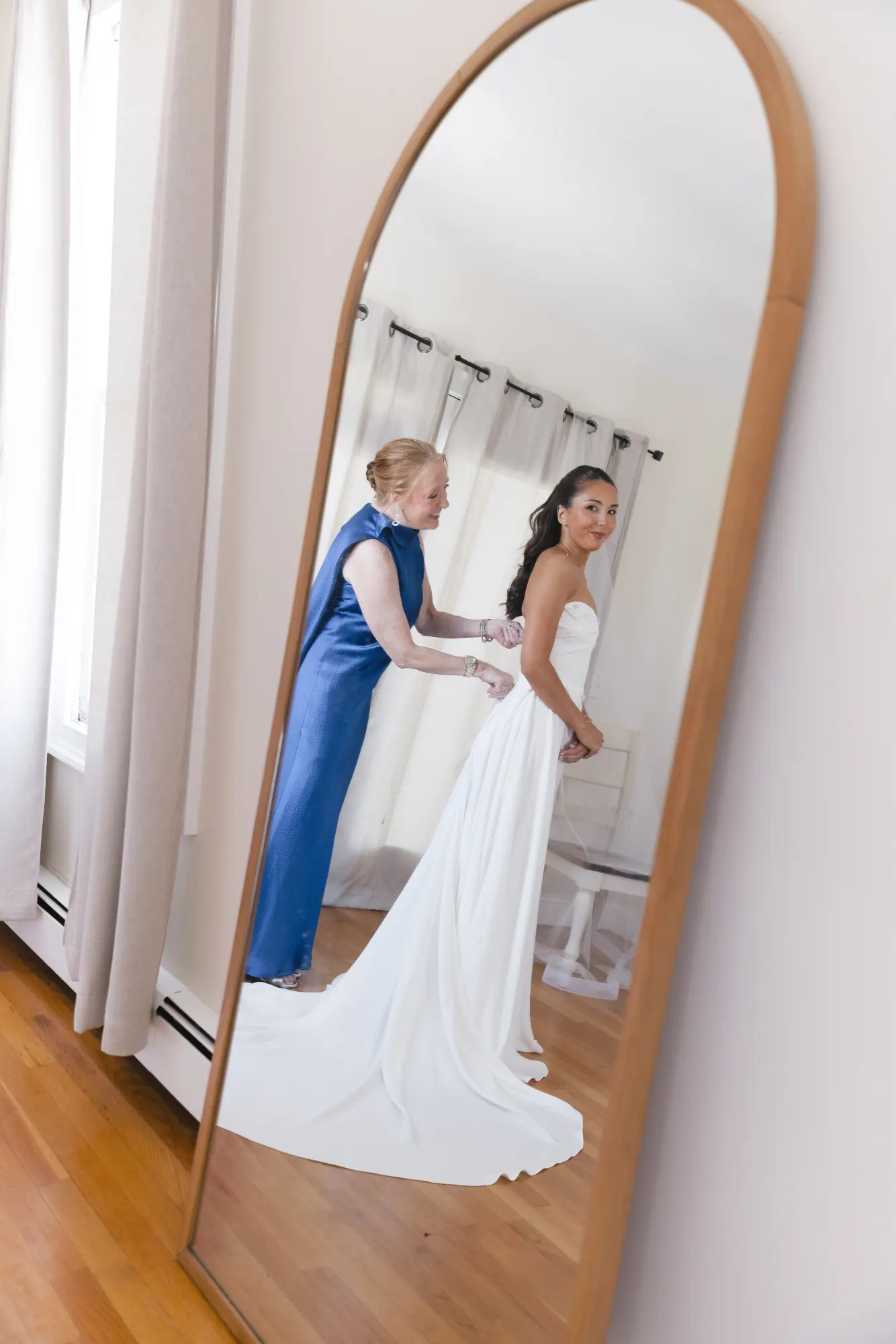 Bride checks her gown in the arched mirror with her mother beside her