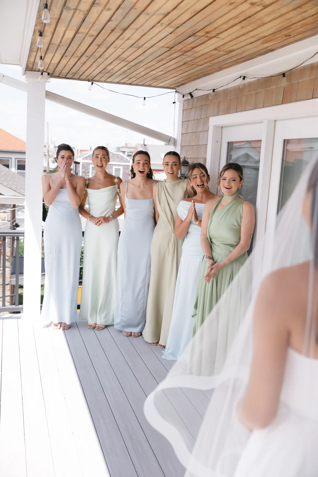 Bridesmaids in pastel gowns see the bride for the first time on the porch