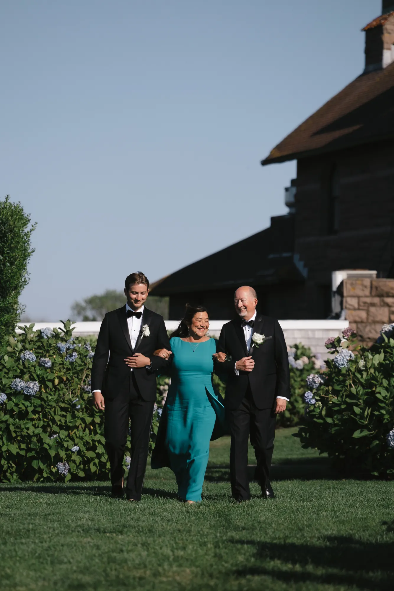Groom walks the aisle escorted by his parents at OceanCliff