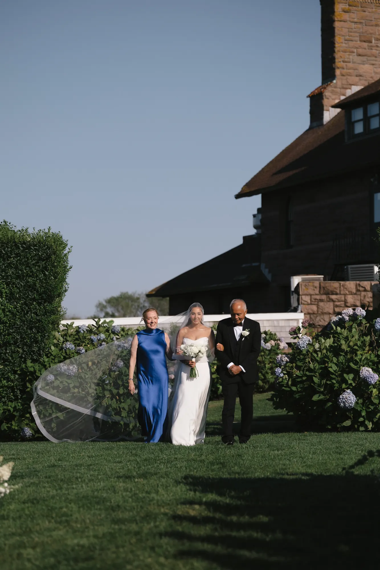 Bride walks the aisle escorted by her parents on the Bridge Lawn