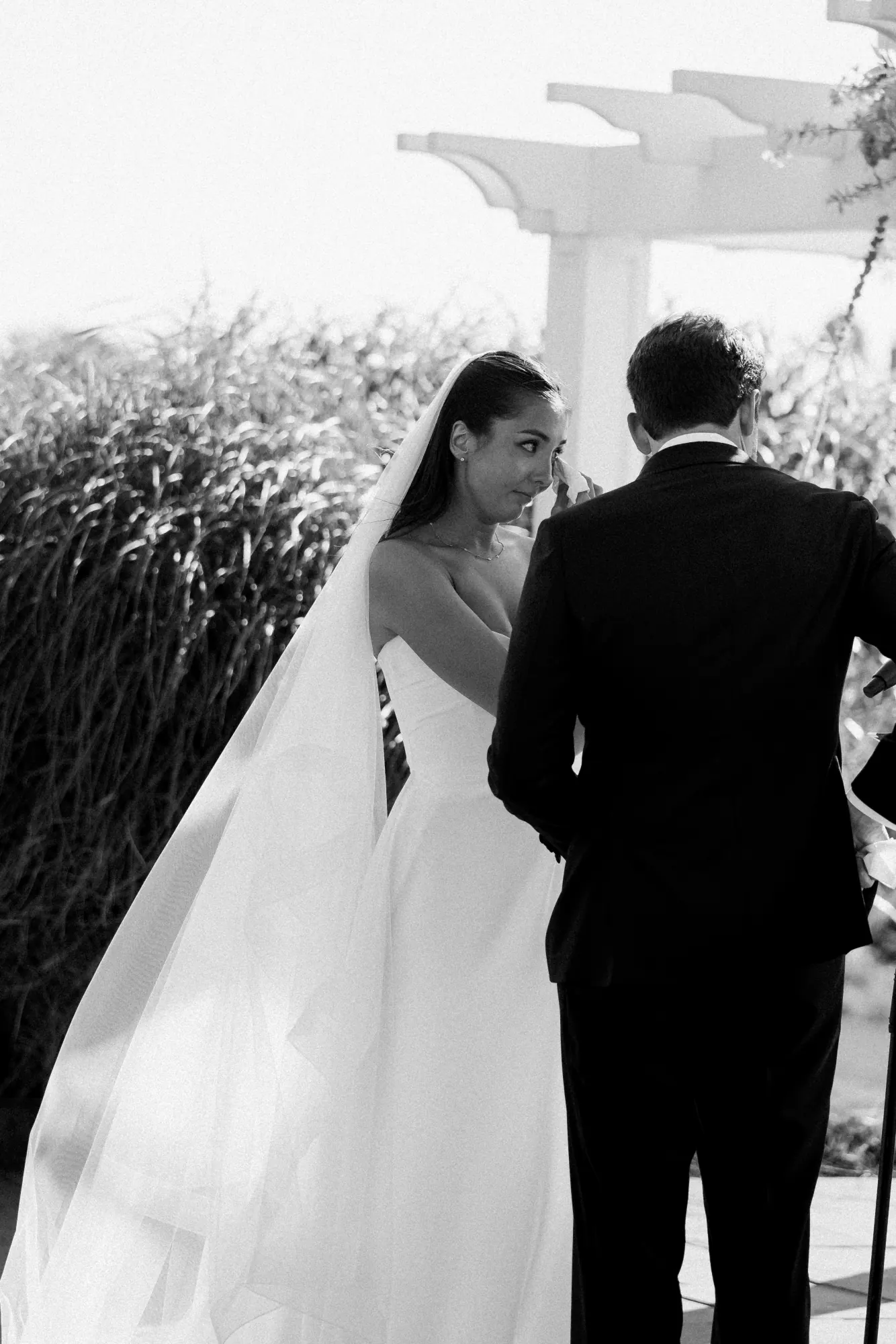 Black and white of the couple at the pergola from behind the seagrass