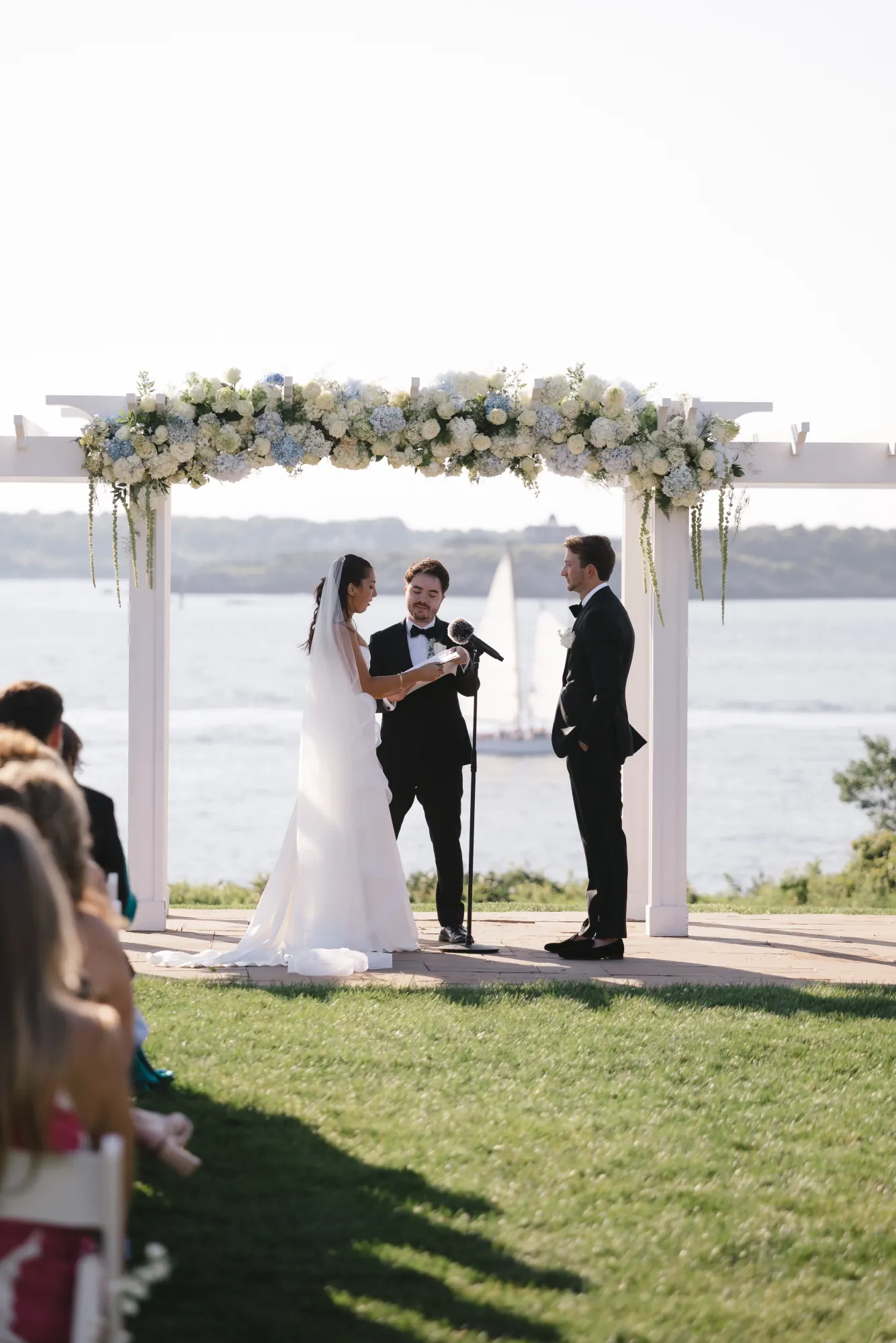 The ceremony framed by the bay and sailboats behind the pergola