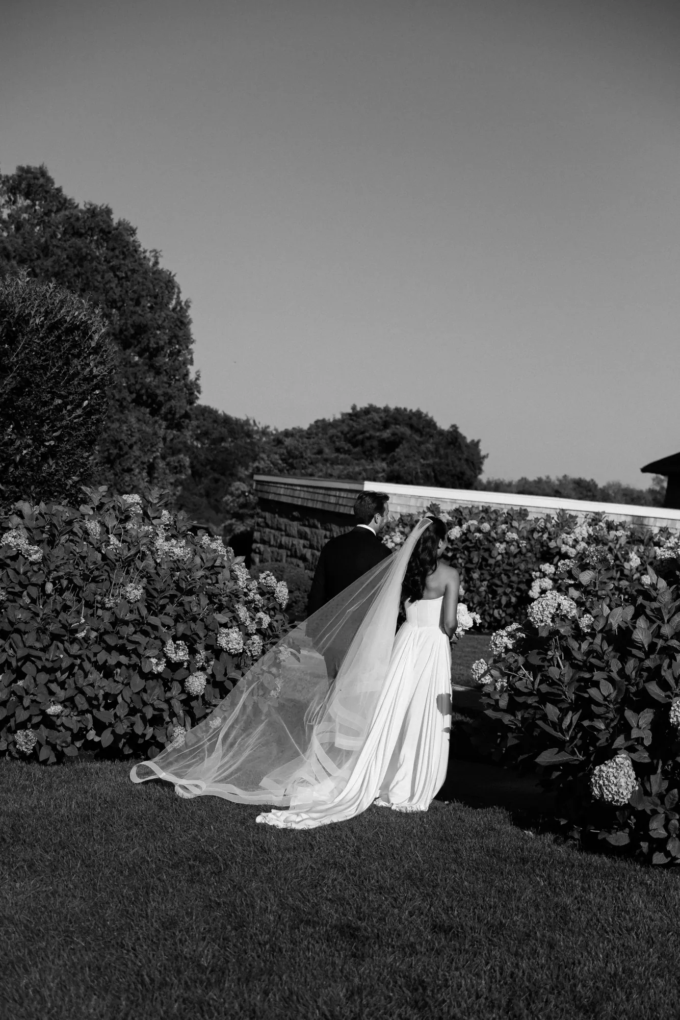 Black and white of the couple walking the hydrangea-lined gardens