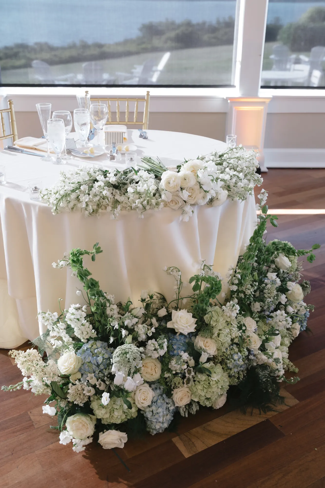 Sweetheart table wrapped in white and blue florals with a bay view