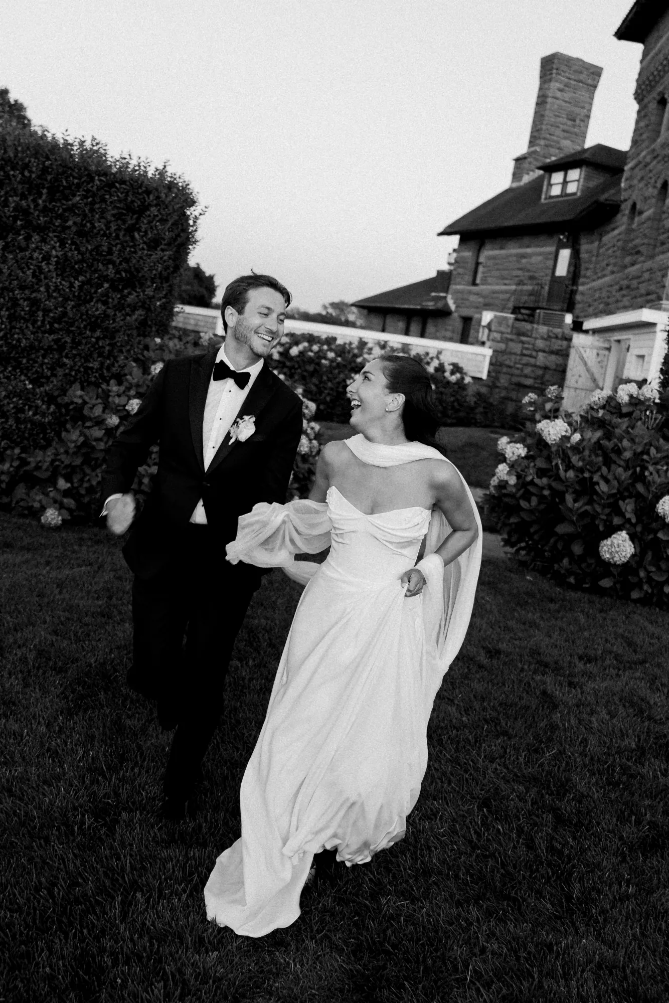 Black and white of the couple laughing across the lawn at dusk