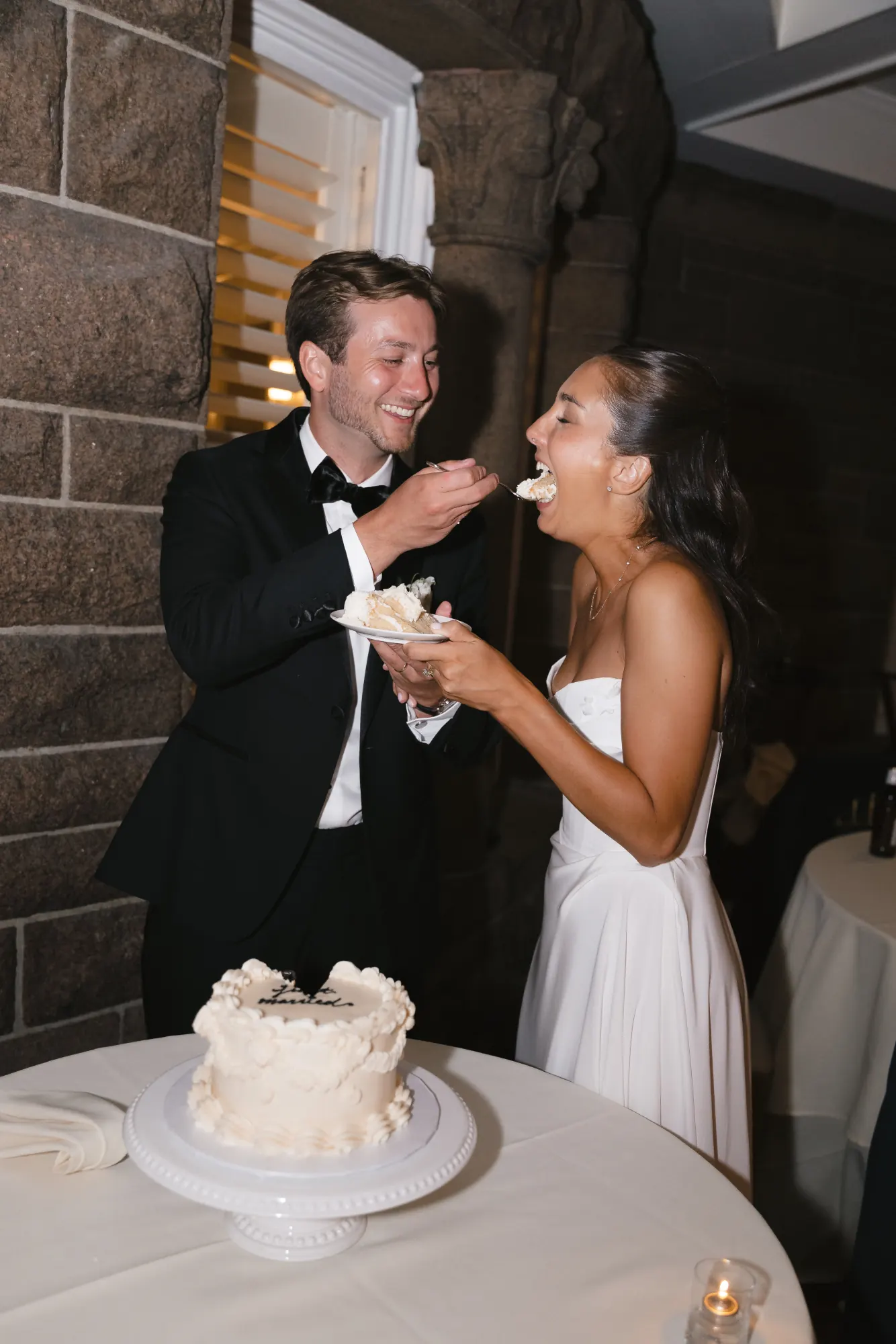 The couple laugh through a bite of wedding cake