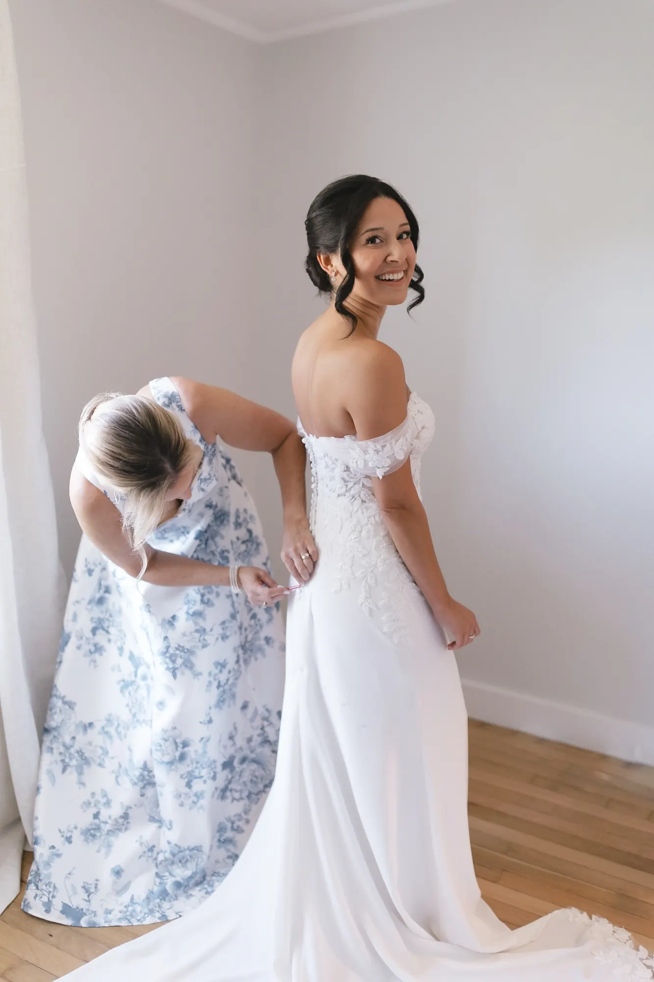 Bride's mother helps her into an off-the-shoulder lace gown before the ceremony