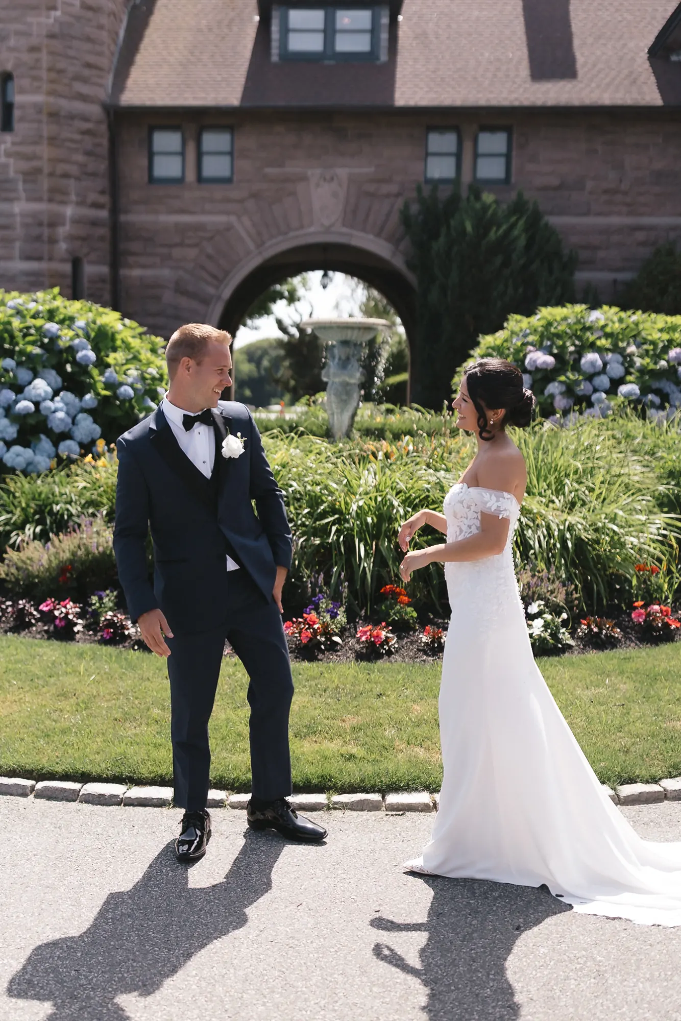 Bride and groom hold hands during their first look in front of the arched OceanCliff mansion