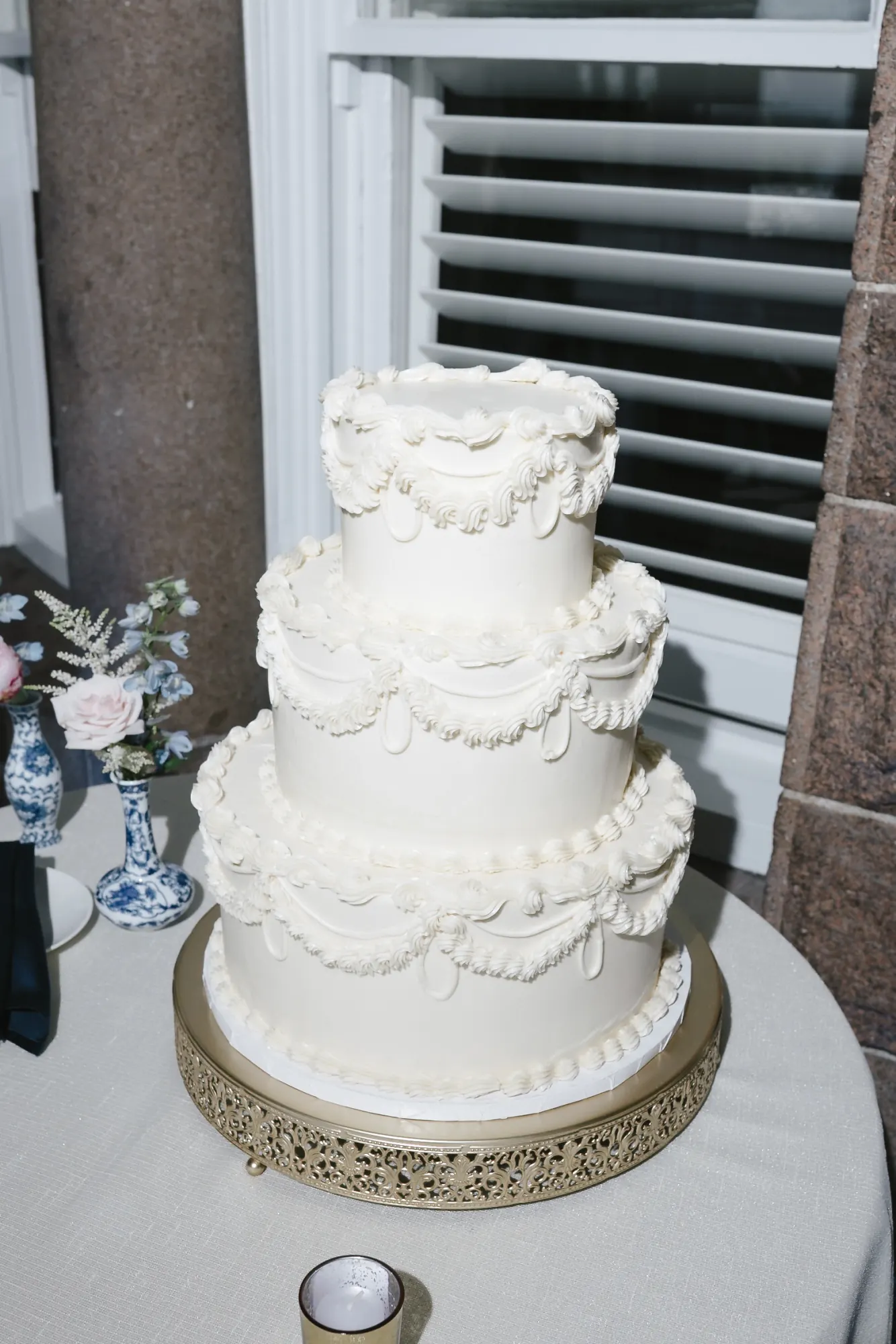 Three-tier white wedding cake with piped scallop detail on a gold stand