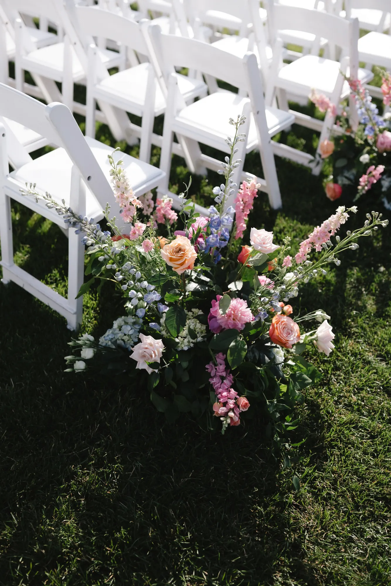 Pastel aisle florals on white folding chairs at the OceanCliff waterfront ceremony