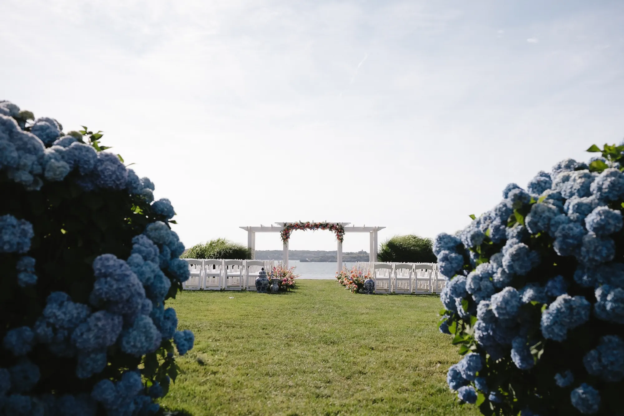 Ceremony arbor framed by blue hydrangeas on the OceanCliff lawn above the bay