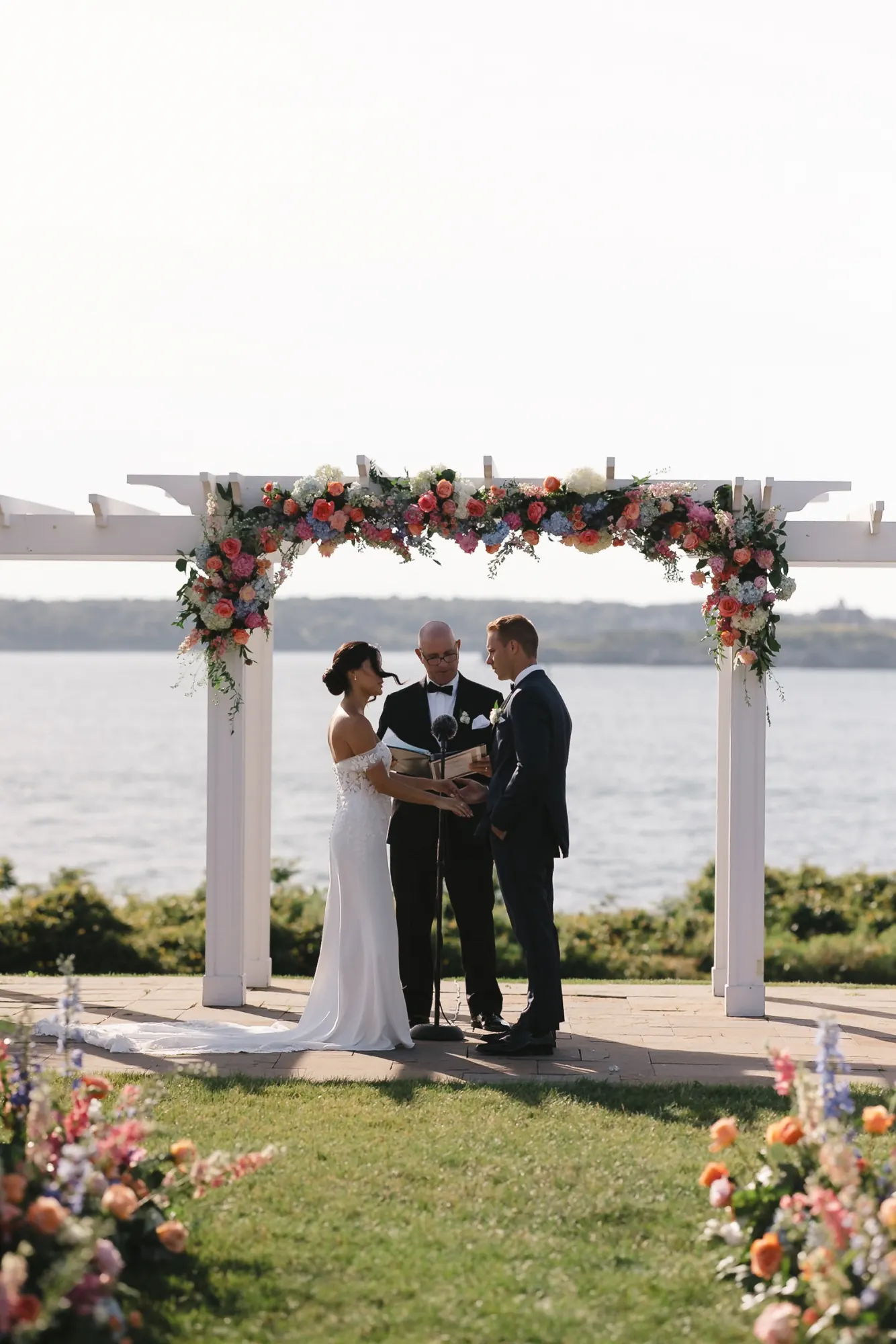 Waterfront wedding ceremony under a floral arbor overlooking Narragansett Bay at OceanCliff