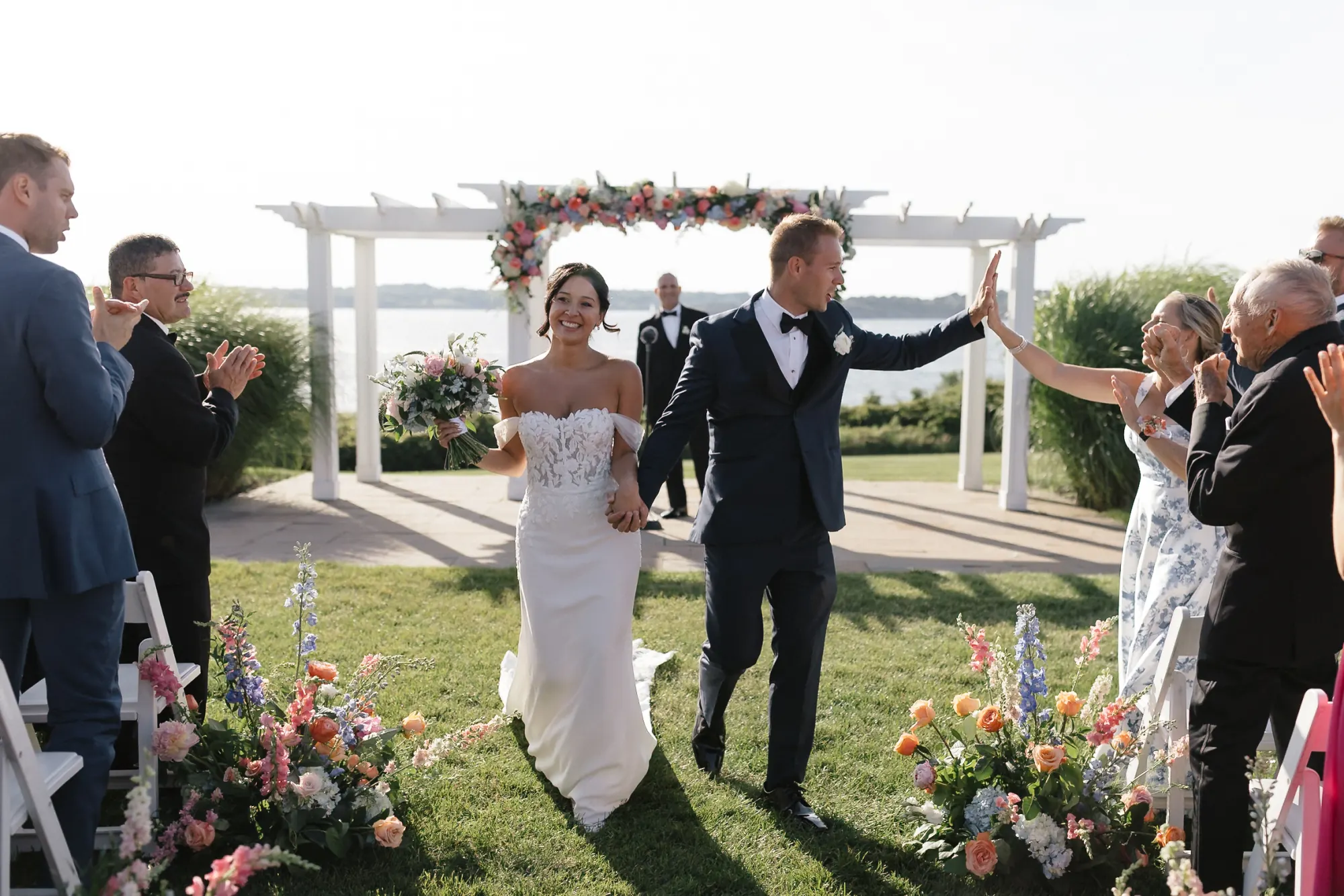 Bride and groom raise their arms during the recessional under the arbor at OceanCliff
