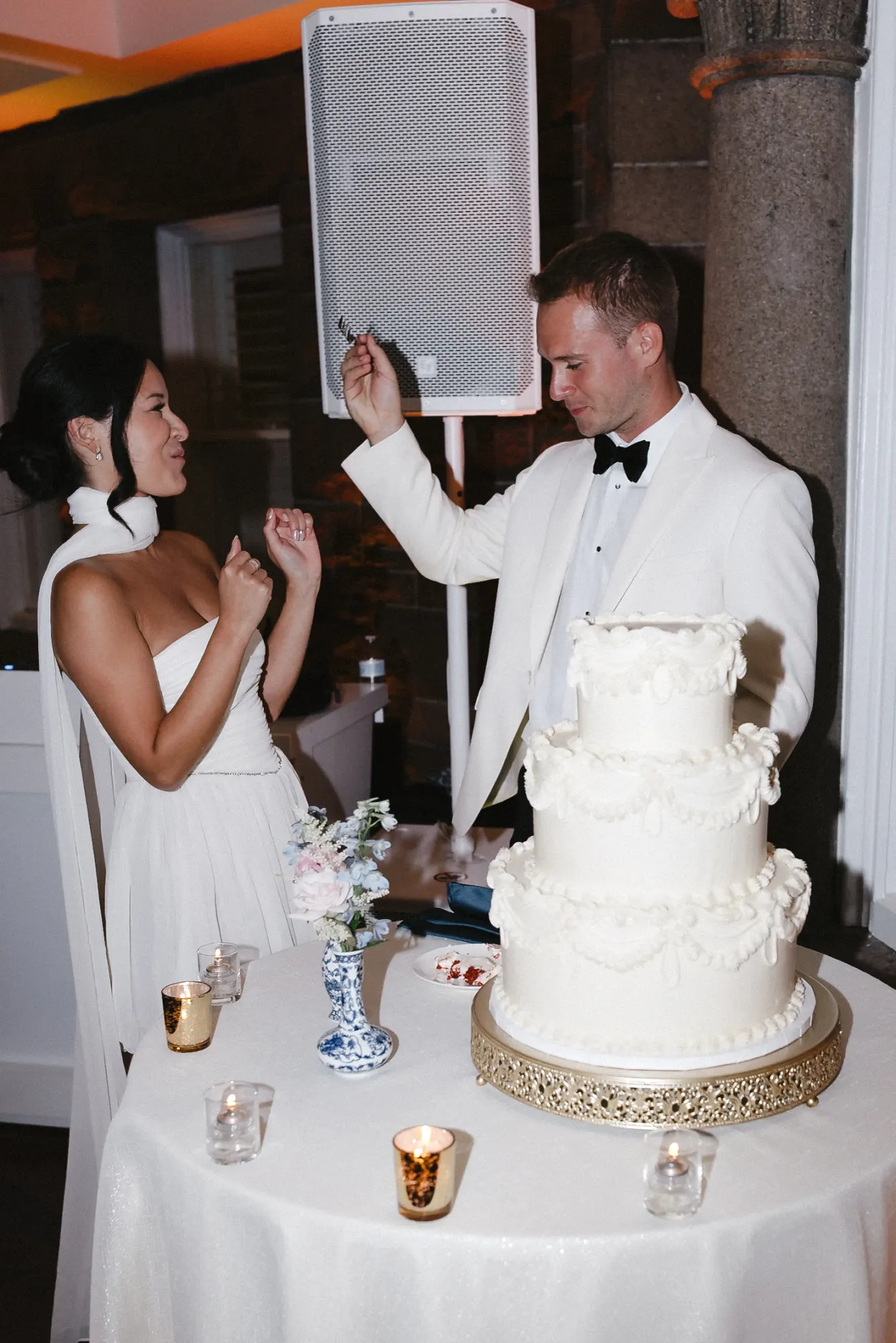 Bride and groom laugh by the cake, the groom now in a white dinner jacket