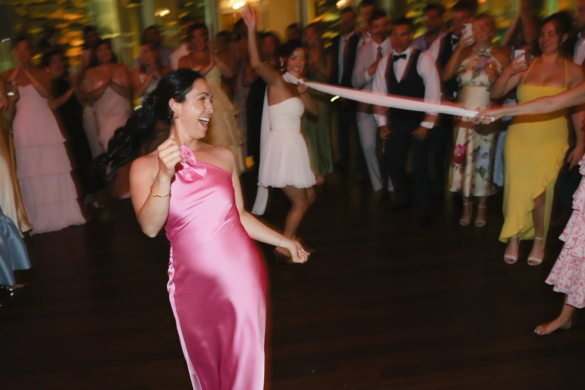 A bridesmaid in a pink satin dress dances at the OceanCliff wedding reception